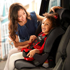 Woman adjusting a child's car seat in a vehicle with a cityscape background