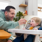 Man feeding a child in a high chair in a kitchen
