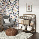 Decorative room with floral wallpaper, metal changing table/shelving unit, and gray armchair.