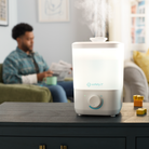 White humidifier on a table with a blurred person reading in the background