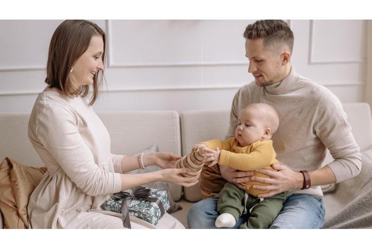 baby playing with toy in dad's lap with mother observing 