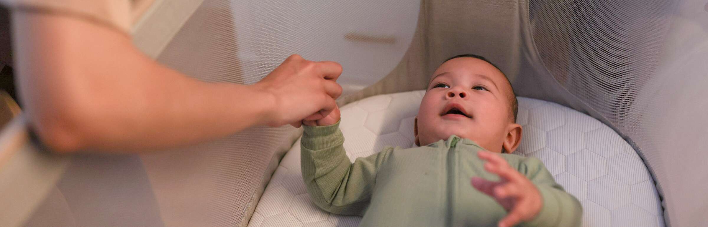 baby in crib with mother holding his hand