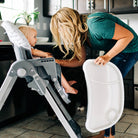 mom holding high chair tray with toddler girl in seat