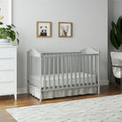 Gray crib in a nursery with white walls, a white dresser, and framed animal prints.
