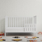 White crib in a room with a patterned wall and toys on the floor.