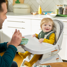 Child in a high chair being fed by an adult in a kitchen setting