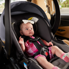 Baby in a car seat with a bow, inside a vehicle.