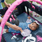 Baby lying on a pink and black play mat with a person's hand reaching out.